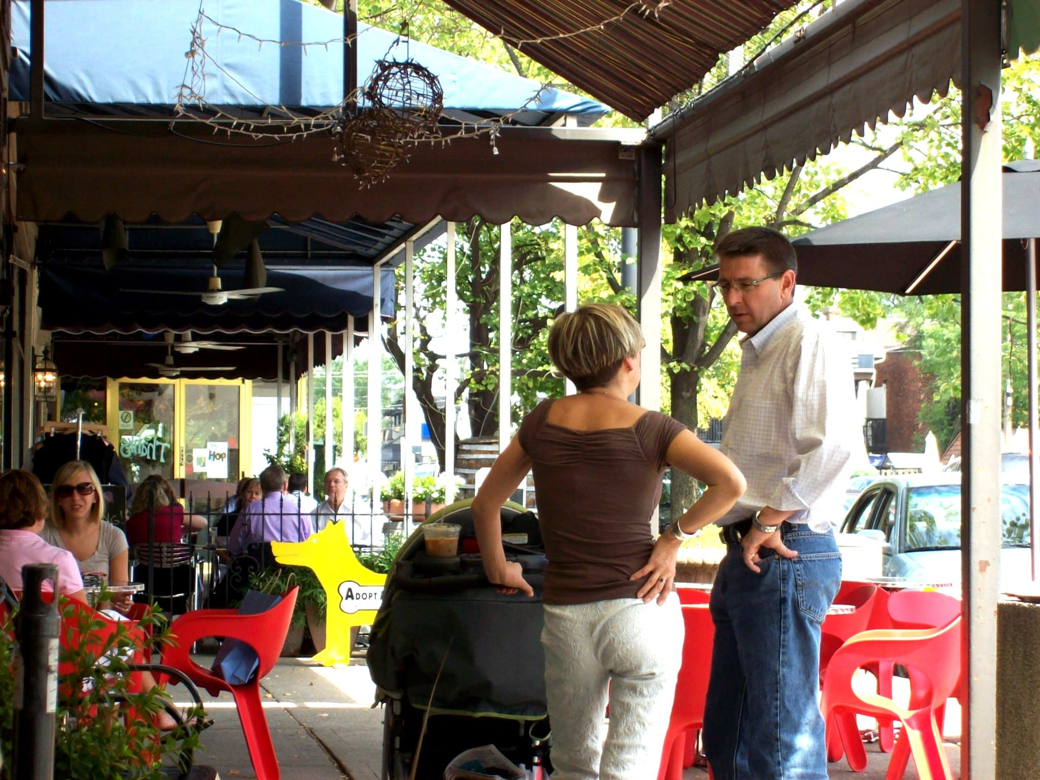 Sunny sidewalk cafe seating under awnings on Grandview Avenue with leafy street trees
